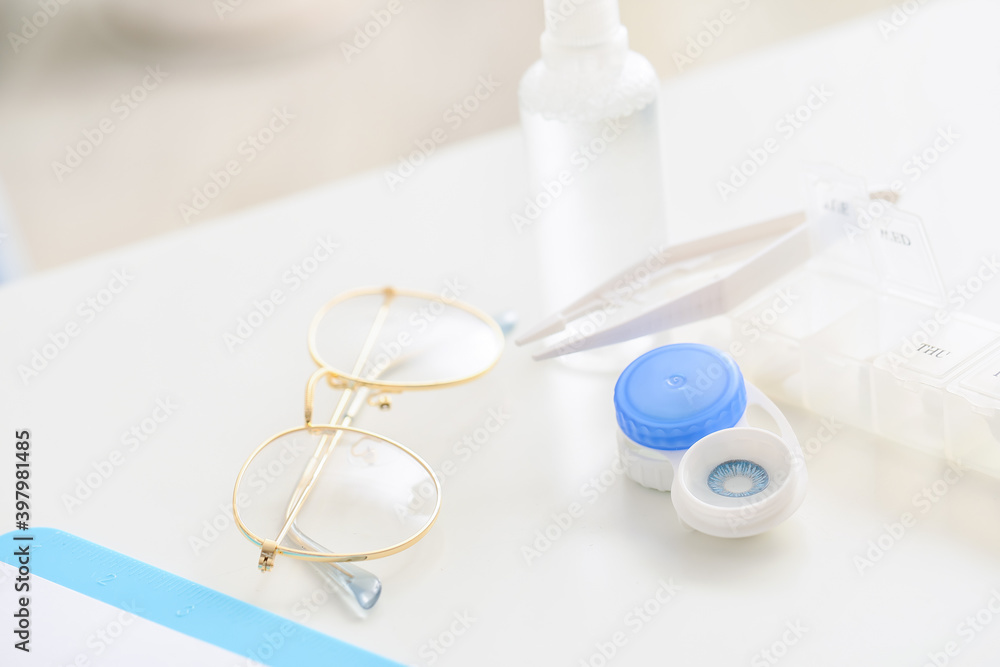 Container with contact lenses, tweezers and glasses on table