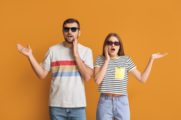 Wall Mural - Surprised couple with stylish sunglasses on color background