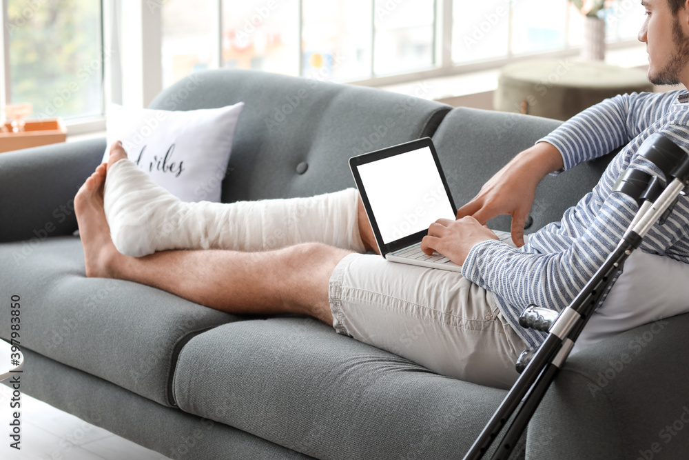 Young man with broken leg using laptop at home