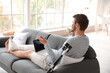 © Pixel-Shot - Young man with broken leg using laptop while talking by phone at home