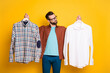 Photo portrait of bearded millennial choosing shirts in fitting room difficult decision isolated on bright yellow color background