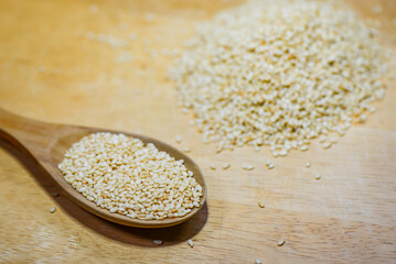 Close-up of a wooden spoon scooping white sesame on a light wooden table. White sesame is an essential ingredient in both savory and sweet Asian dishes.