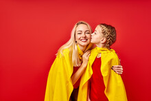 Woman And Child Girl In Superhero Costumes Posing At Camera Isolated Over Red Background, Cute Child Girl Kisses Mother On Cheek, Love Concept