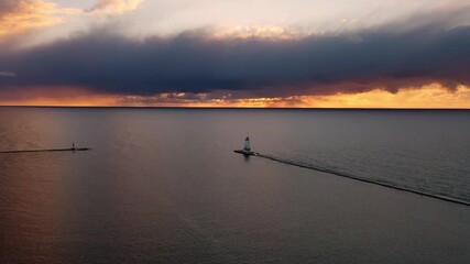 Wall Mural - Beautiful panning out sunset aerial of the white colored Ludington breakwater lighthouse with blue and orange sky and clouds above reflecting on the tranquil or calm water of Lake Michigan.