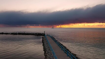 Wall Mural - Beautiful sunset aerial panning over a pier looking towards the white colored Ludington breakwater lighthouse with pink and orange sky and clouds above reflecting on the water of Lake Michigan.
