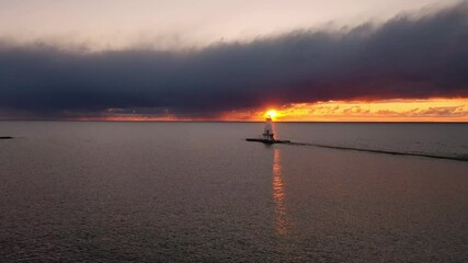 Wall Mural - Sunset aerial flying towards the Ludington breakwater lighthouse as the bright yellow sun shines from below the clouds creating a beautiful orange sky and reflection on the water.
