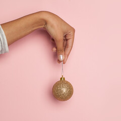 Wall Mural - Golden Christmas ball decoration in female hand on pastel pink card background