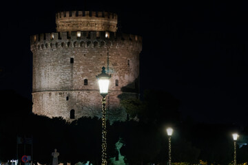 Thessaloniki Greece night view of The White Tower with Christmas lights decoration around. The city's landmark with illuminated seasonal instalments under dark sky.