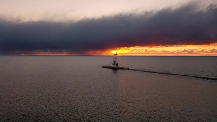 Wall Mural - Beautiful panning aerial of the Ludington Breakwater Lighthouse with the bright orange and yellow sun shining behind the structure, reflecting on the water and lighting up the clouds in sky at sunset.