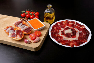 Breakfast with bread toasts with acorn-fed Iberian ham, tomato, garlic and olive oil (tumaca bread) with black background