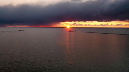 Wall Mural - Beautiful sunset aerial panning in towards the white colored Ludington breakwater lighthouse with pink, yellow and orange sky and sun and clouds above reflecting on the calm water of Lake Michigan.