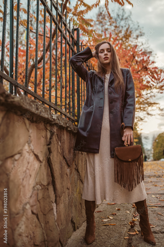 Elegant fashionable lady wearing trendy faux leather trench coat, jersey midi  dress, high boots, holding brown suede handbag with fringe, posing in  street. Outdoor autumn fashion full-length portrait Stock Photo | Adobe