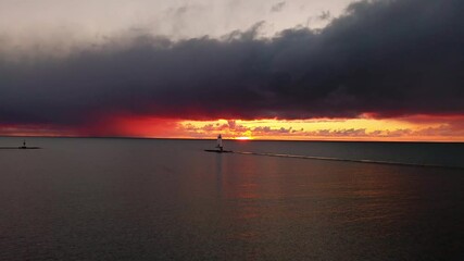 Wall Mural - Beautiful panning in aerial of the Ludington Breakwater Lighthouse with the sun reflecting on the water of Lake Michigan and lighting up the sky and clouds with colorful pink, orange and yellow.