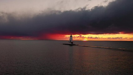 Wall Mural - Beautiful colorful sunset aerial of the white Ludington breakwater lighthouse as birds fly by the pink and orange sky as the sun lowers below the horizon reflecting on the water of Lake Michigan.