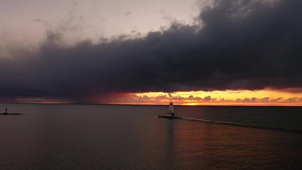 Wall Mural - Beautiful panning sunset aerial of the white colored Ludington breakwater lighthouse with pink and orange sky and clouds above reflecting on the calm or tranquil water of Lake Michigan.