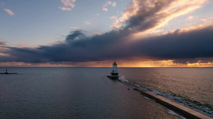 Wall Mural - Beautiful sunset aerial panning over the breakwater wall as waves splash up and a bird flies by with the Ludington lighthouse at the end of the pier in front of a blue and orange colored sunset sky.