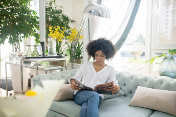 Smiling young woman reading magazine in cozy room