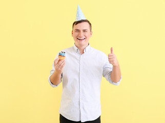 Poster - Young man with birthday cupcake showing thumb-up on color background