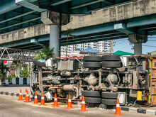 A View Of Under The Truck Carrying A Container Overturned On A Road Under A Bridge Over An Intersection.