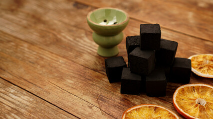 Coals for hookah on wooden background with dry oranges and bowl. Place for text