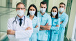 © My Ocean studio - Serious confident doctors team in safety medical masks with crossed arms are looking on the camera on hospital background