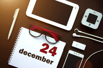 December 24th. Day 24 of month, Calendar date. Office workplace with laptop, notebook, office supplies and stationery on brown back. Winter month, day of the year concept.