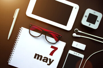 May 7th. Day 7 of month, Calendar date. Office workplace with laptop, notebook, office supplies and stationery on brown back. Spring month, day of the year concept.