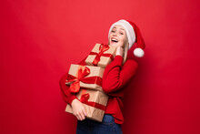 Excited Surprised Woman In Red Santa Claus Outfit Holding Stack Presents Isolated On The Red Background