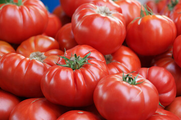 Red ripe tomatoes background. Pile of fresh organic vegetables on sale at grocery store, close up view. Vegetarian food concept.