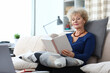© H_Ko - Adult woman sit on sofa at home, rest and read book alone.