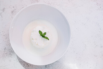 Wall Mural - Fromage blanc de brebis frais et petit lait avec une feuille de menthe dans un bol blanc