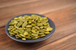 Pumpkin seeds pile in black plate on wooden background. Recipe, nutrition, diet concept. Close-up, copy space