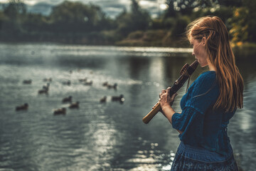 beautiful shamanic girl playing on shaman flute in the nature.