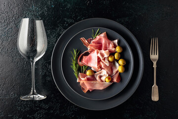 Wall Mural - Prosciutto, green olives and rosemary on a black plate.