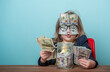 © shara - Education for kids how to be rich. Child with dollar bills shoved over glasses covering eyes. Financial independence and ability to earn a lot of money. Back to school