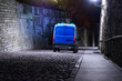 A blue and white police van speeding in a narrow medieval cobblestone city street in the night