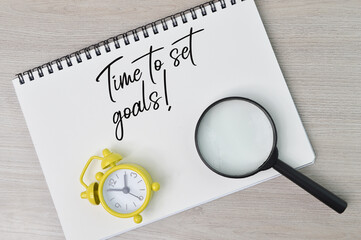 Top view of magnifying glass, clock and notebook written with text TIME TO SET GOALS!. Business and education concept.