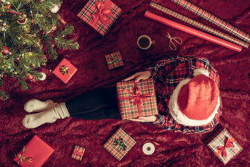 Wall Mural - Top view of woman with christmas gift box on knees. Female wrapping gifts for family sitting on fluffy plaid near christmas tree. Flat lay.