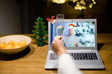 Female Hand With A Glass Of Champagne In Cheers Gesture, A Man In Santa Hat On The Laptop Screen Smiles. Celebrating Christmas Eve Via Video Call, Virtual Party