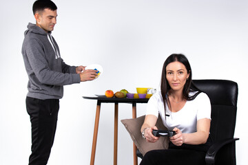 A focused woman is playing a game while her boyfriend is cleaning the dishes. White background and gender stereotypes.