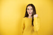 © Irene - Pretty girl wearing a yellow sweater standing over isolated yellow background angry and mad raising fist frustrated and furious while shouting with anger.
