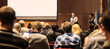 © kasto - Speaker giving a talk in conference hall at business meeting event. Rear view of unrecognizable people in audience at the conference hall. Business and entrepreneurship concept.