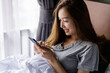 © Rattanachoat - Beautiful long hair women play smartphone on the bed after wake up in the morning.