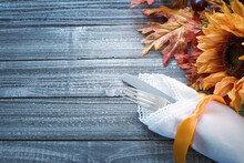 Fall Thanksgiving Table Setting On Rustic Wood Boards With Silverware, White Napkin, Sunflower And Autumn Leaves On Side With Copy Space.  It's Horizontal With Above View.