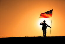 Silhouette Of USA Armed Forces Soldier, Army Infantryman Or Marine Corps Fighter Veteran Saluting While Standing With National Flag On Sunset Background. Military Victory And Glory, Fallen Remembrance