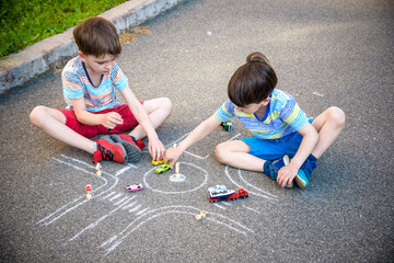 Two brothers sibling kid boy having fun with picture drawing traffic car with chalks. Creative leisure for children outdoors in summer. Difficult traffic rules education friendship concept