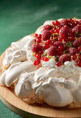 Wall Mural - food, culinary, baking and cooking concept - close up of pavlova meringue cake decorated with red berries on wooden serving board