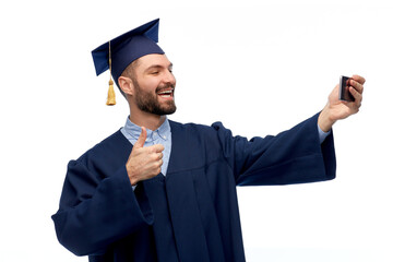 Poster - education, graduation and people concept - happy smiling male graduate student in mortar board and bachelor gown with smartphone having video call or taking selfie over white background