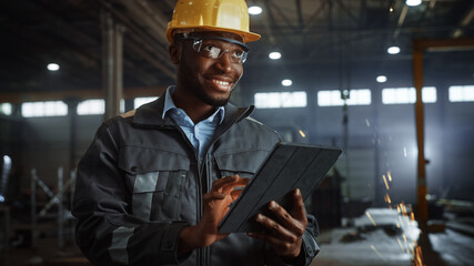 Aufkleber - Professional Heavy Industry Engineer/Worker Wearing Safety Uniform and Hard Hat Uses Tablet Computer. Smiling African American Industrial Specialist Standing in a Metal Construction Manufacture.