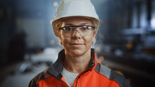 Portrait Of A Professional Heavy Industry Engineer Worker Wearing Uniform, Glasses And Hard Hat In A Steel Factory. Beautiful Female Industrial Specialist Standing In Metal Construction Facility.